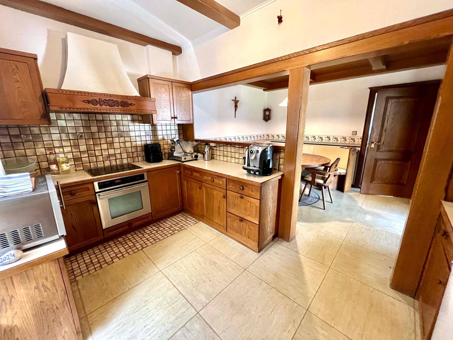 Rustikale Küche mit Holzschränken, gefliestem Spritzschutz und Blick auf den angrenzenden Essbereich.