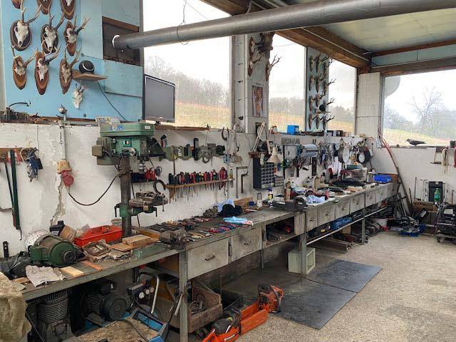 Gut ausgestattete Werkstatt mit zahlreichen Werkzeugen, großer Arbeitsfläche und Jagdtrophäen an der Wand.