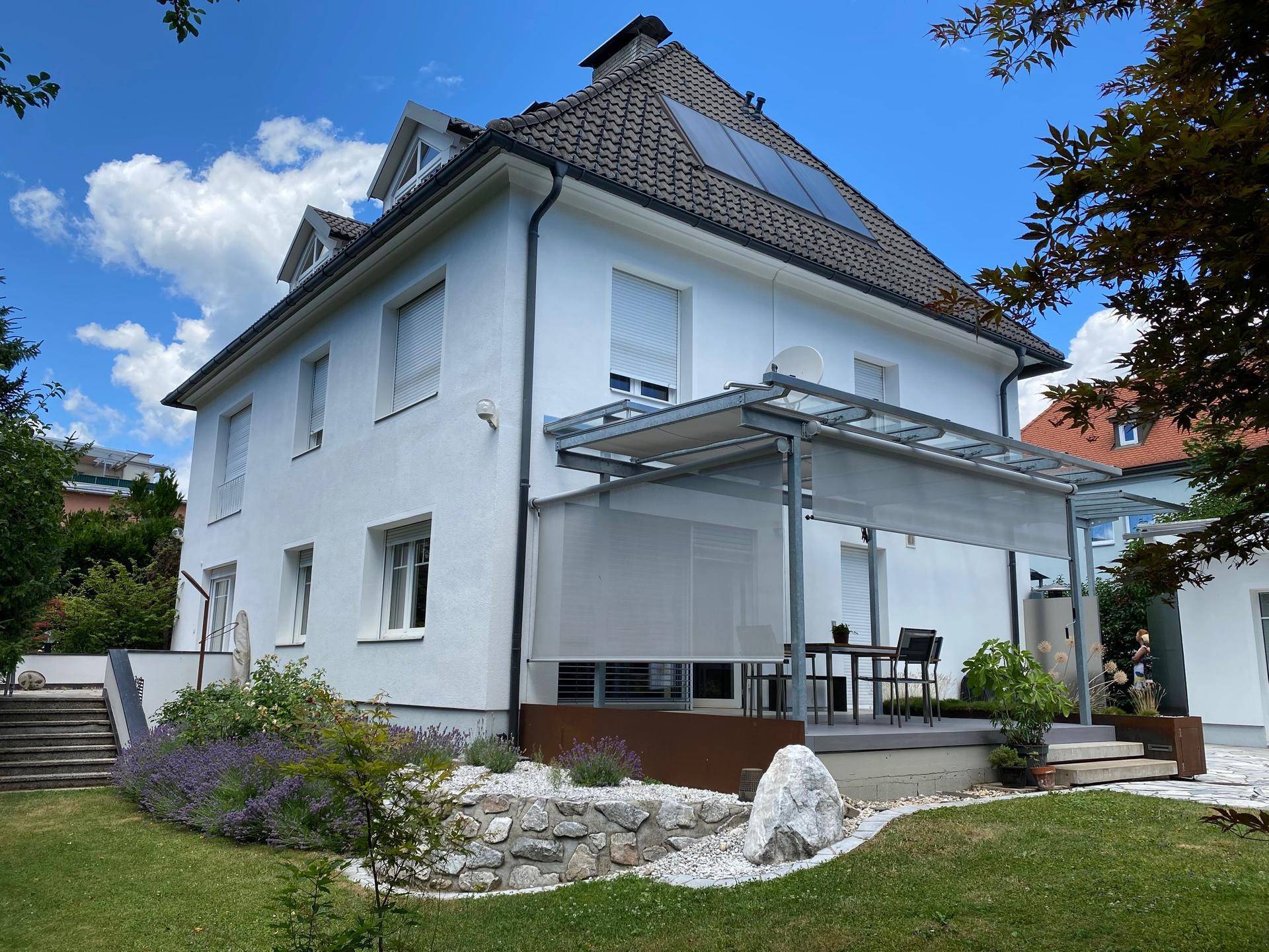 Haus mit möblierter Terrasse, Sonnenschutz und gepflegtem Garten mit Lavendelpflanzen.