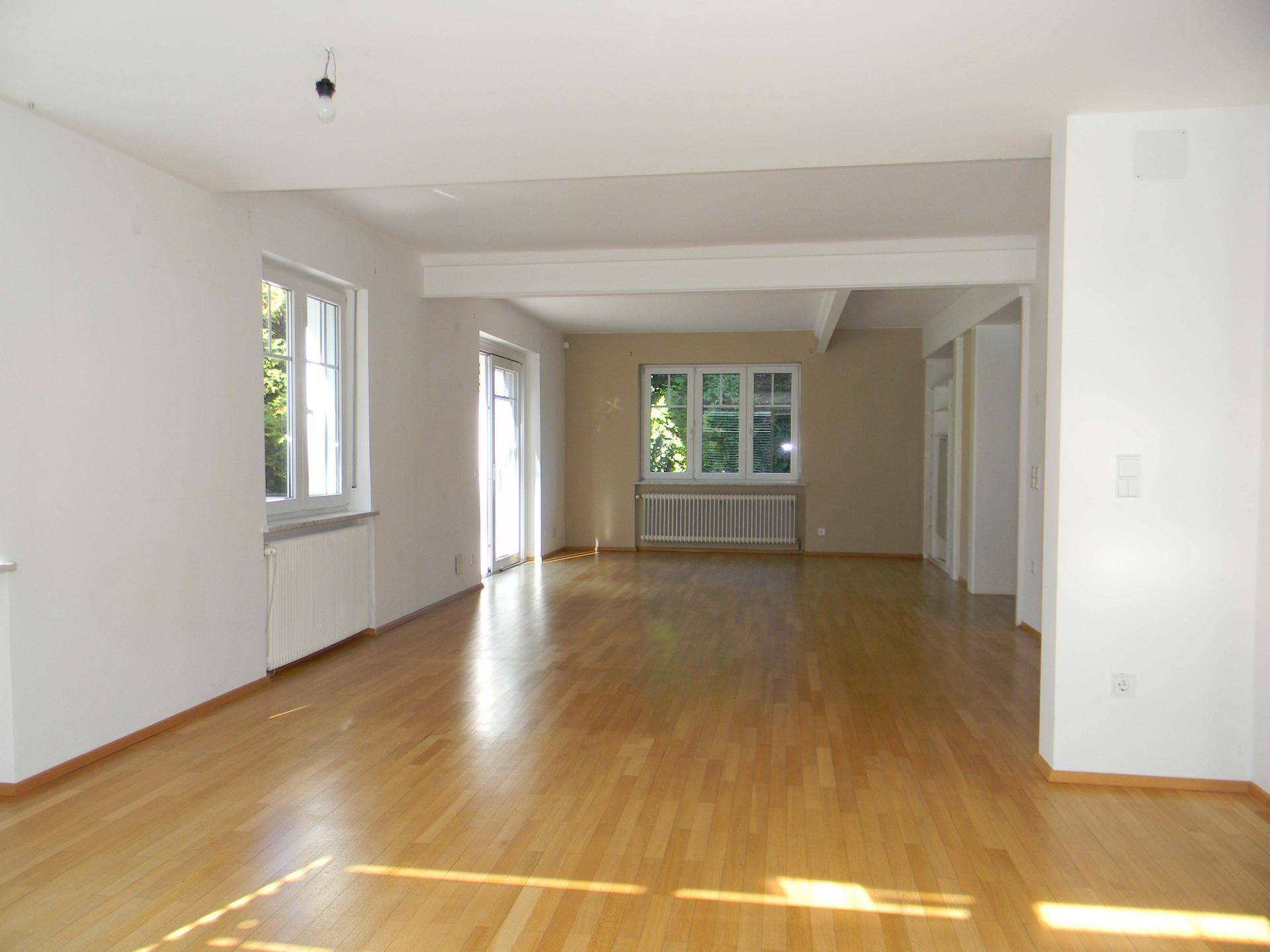 Geräumiges, helles Wohnzimmer mit Holzparkettboden und großen Fenstern zum Garten.