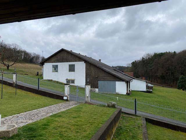 Blick auf ein Nebengebäude und die hügelige Landschaft mit grünen Wiesen unter bewölktem Himmel.
