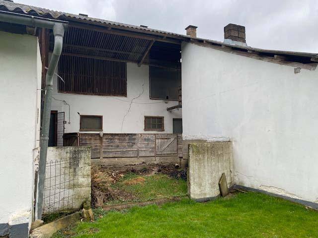 Rückansicht eines Gebäudes mit abfallendem Gelände, alter Holzverkleidung und Grünfläche.