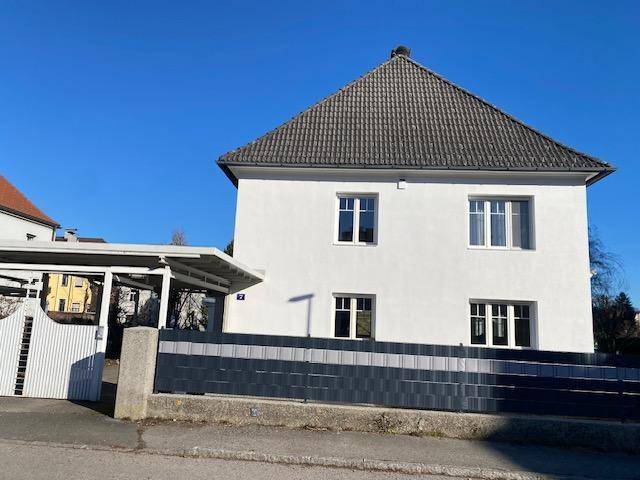 Vorderansicht des weißen Hauses mit dunklem Dach und modernem Zaun unter blauem Himmel.