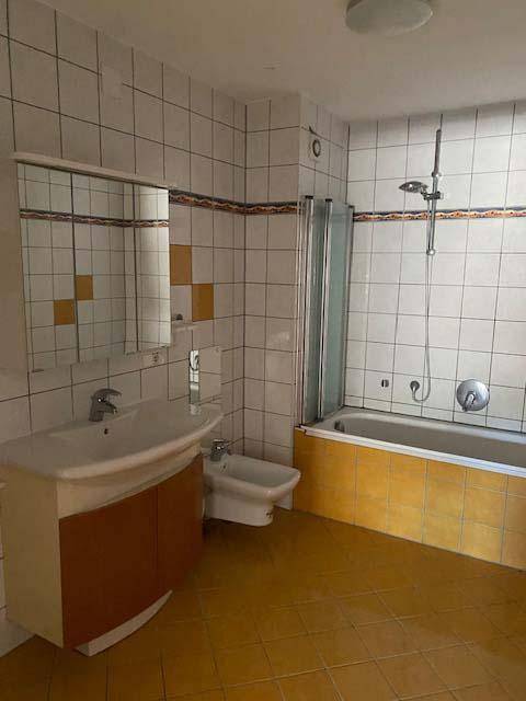Badezimmer mit gelben Bodenfliesen, Badewanne mit Duschabtrennung und Bidet.