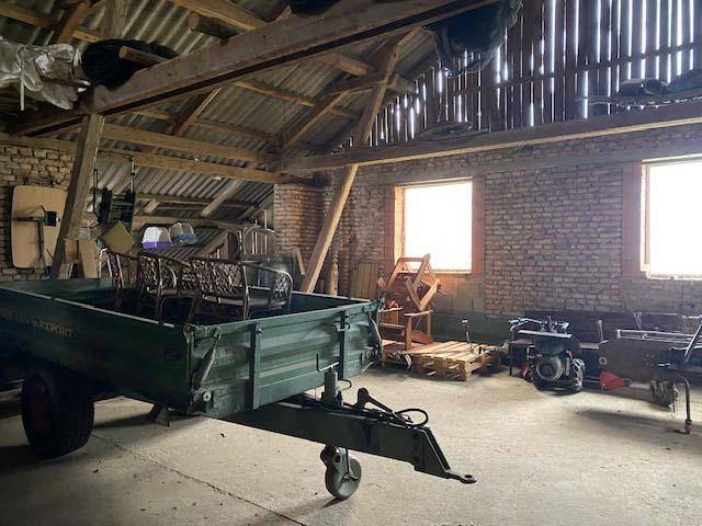 Geräumiger Lagerbereich in einer Scheune mit Anhänger, alten Möbeln und sichtbaren Ziegelwänden.