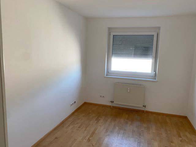 Leeres Schlafzimmer mit hellem Parkettboden, weiß gestrichenen Wänden und Fenster.