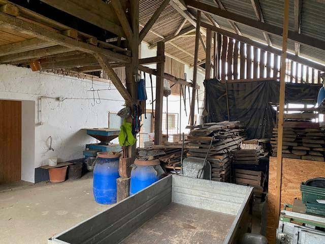 Geräumiger Innenraum einer Scheune mit sichtbaren Holzbalken und landwirtschaftlichen Geräten.