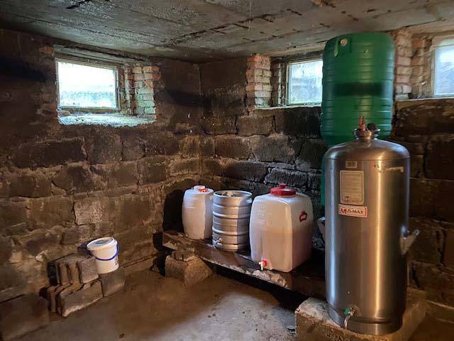 Historischer Steinkeller mit kleinen Fenstern und verschiedenen Behältern für Lagerzwecke.