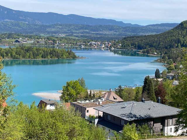 Klarer Blick auf den See mit hellblauem Wasser, umgeben von grünen Hügeln und Bergen.