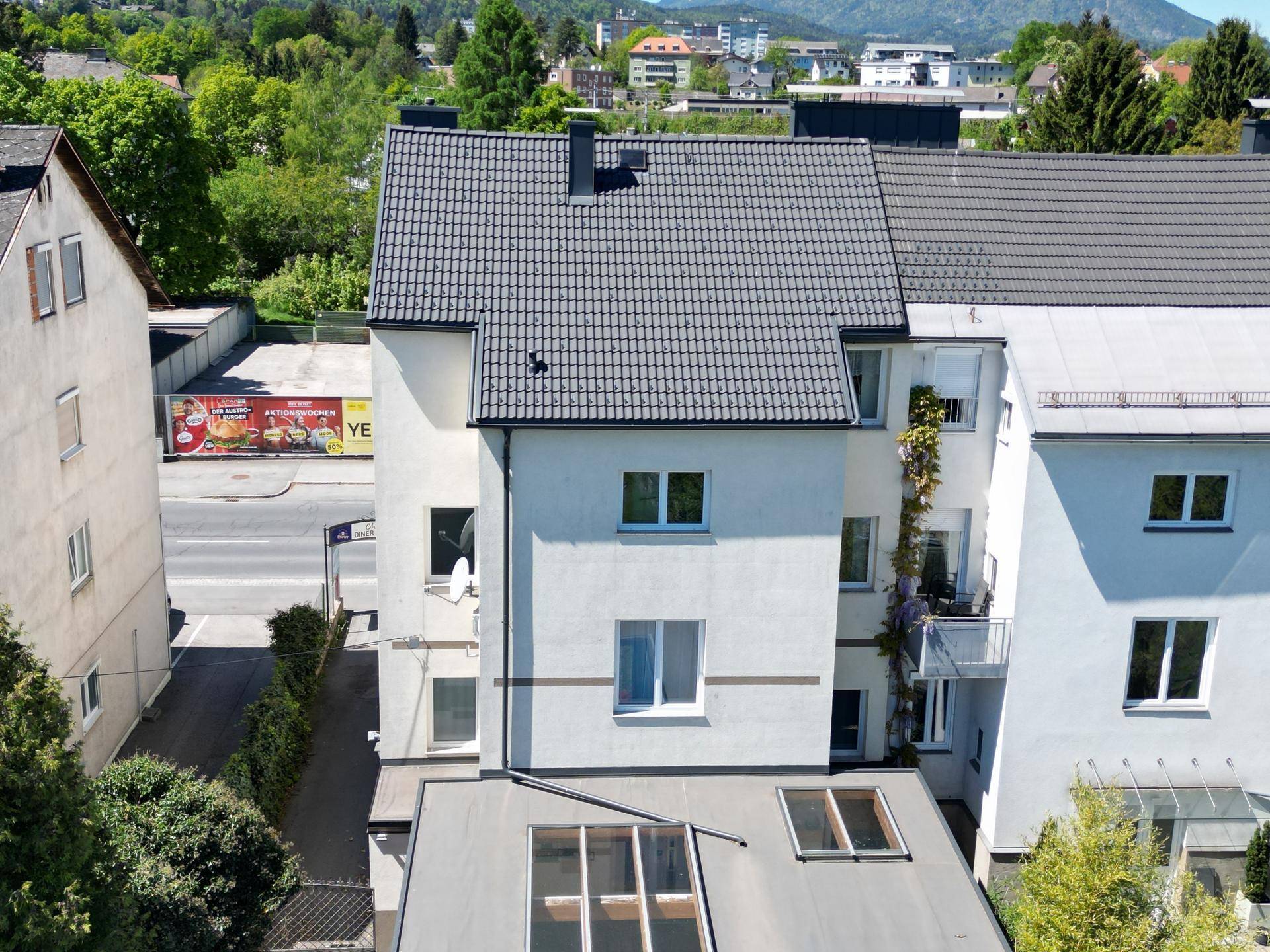 Rückansicht des Gebäudes mit Blick auf die umliegende Bebauung und grüne Hügel.