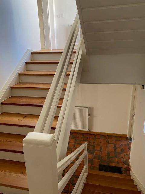 Holztreppe mit weißem Geländer führt zu einem Flur mit Terrakotta-Fliesenboden.