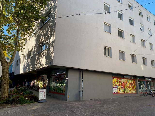 Seitenansicht eines Mehrfamilienhauses mit Geschäften im Erdgeschoss und vielen Fenstern.