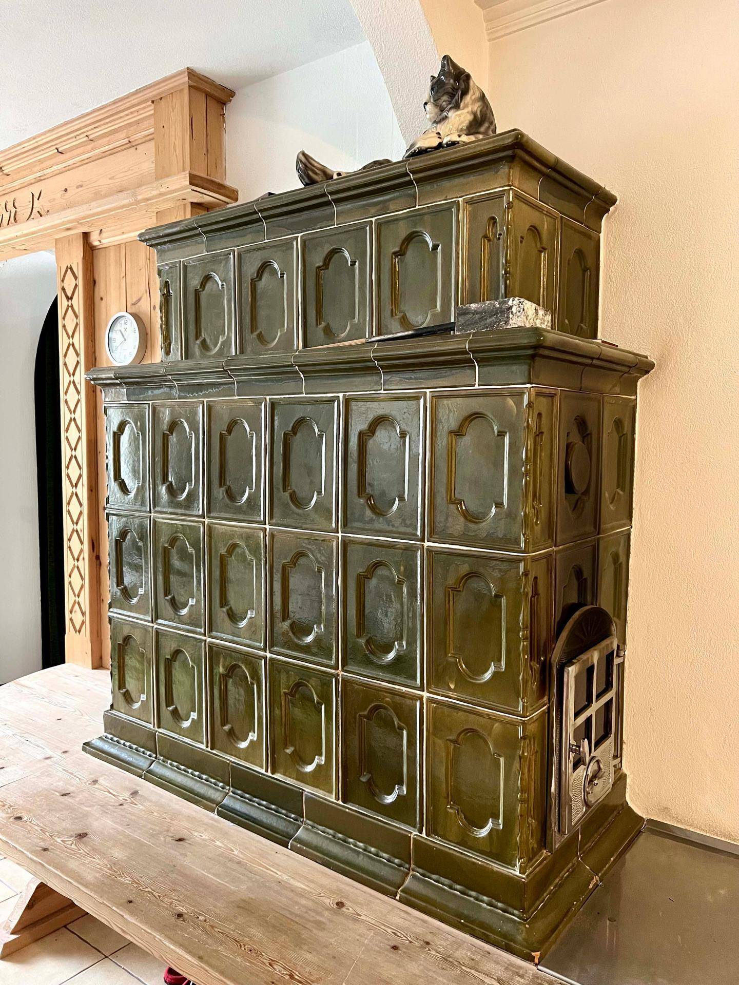 Detailaufnahme des großen, traditionellen Kachelofens mit grünen Fliesen und dekorativen Elementen.