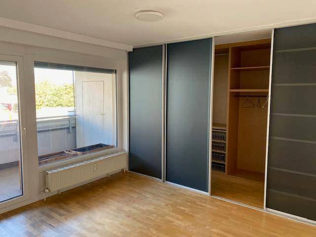 Schlafzimmer mit hellem Parkettboden, Einbauschränken und Zugang zum Balkon.