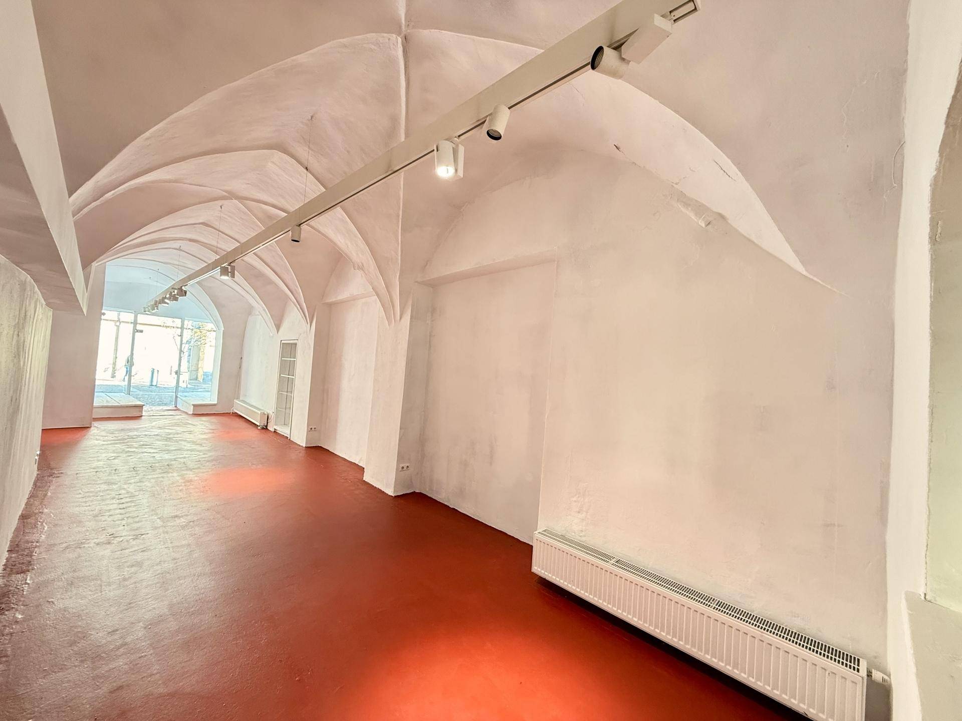 Blick in den Ladenraum mit Gewölbedecken, rotem Boden und Heizkörpern unter den Fenstern.