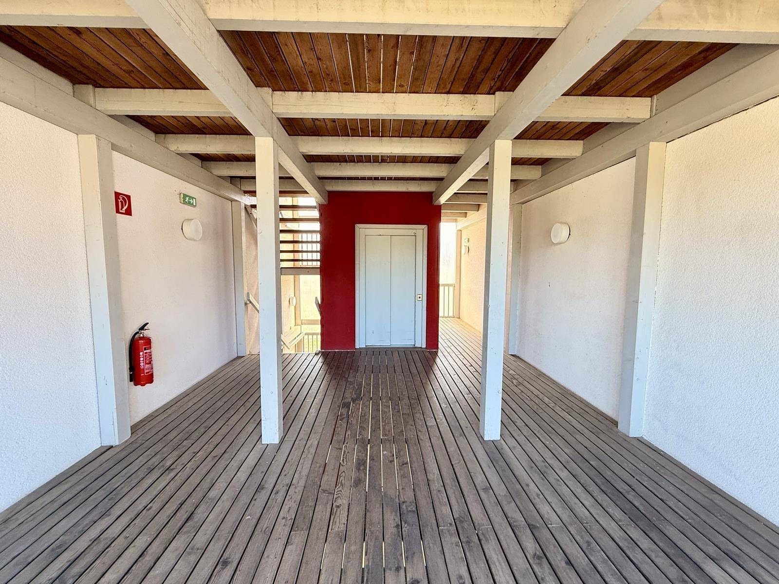 Heller Gemeinschaftsflur mit Holzboden, roter Akzentwand und einem Aufzug.
