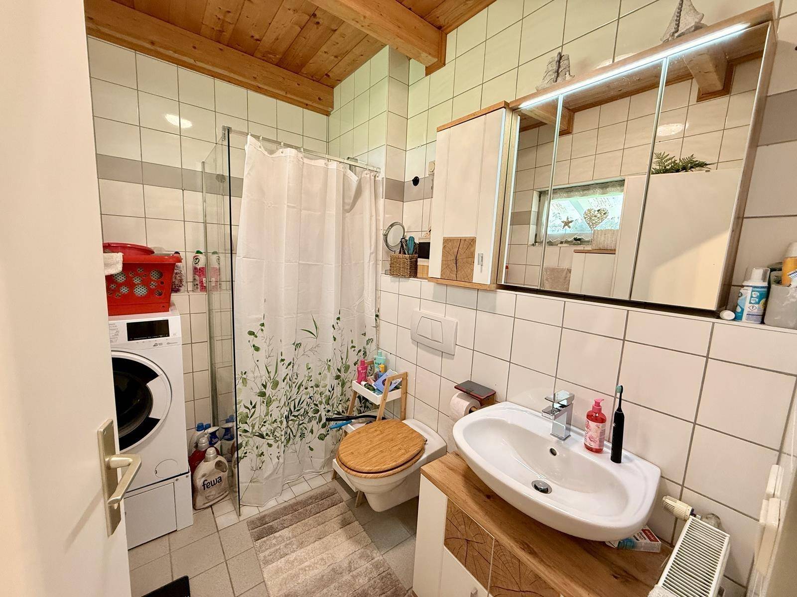 Funktionales Badezimmer mit Dusche, WC, Waschbecken und integrierter Waschmaschine.