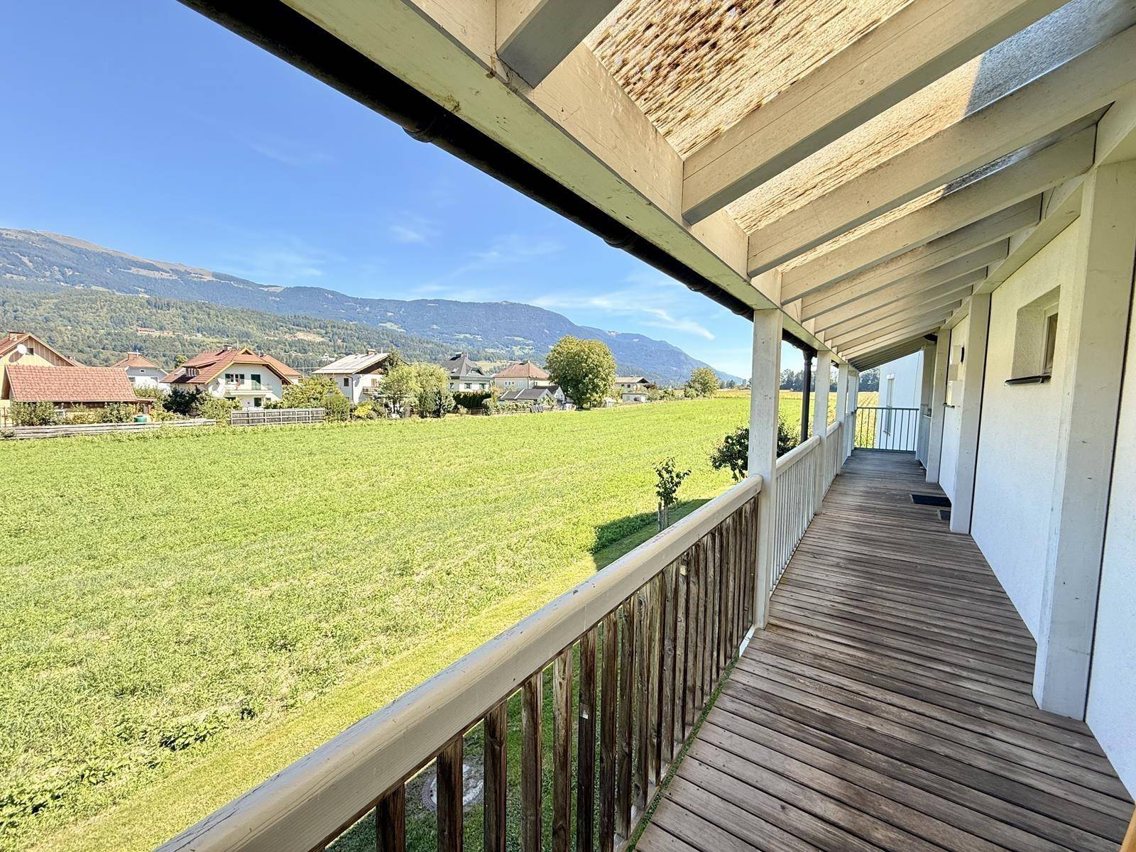 Langer Holzbalkon mit weitem Blick über grüne Felder und die umliegende Berglandschaft.