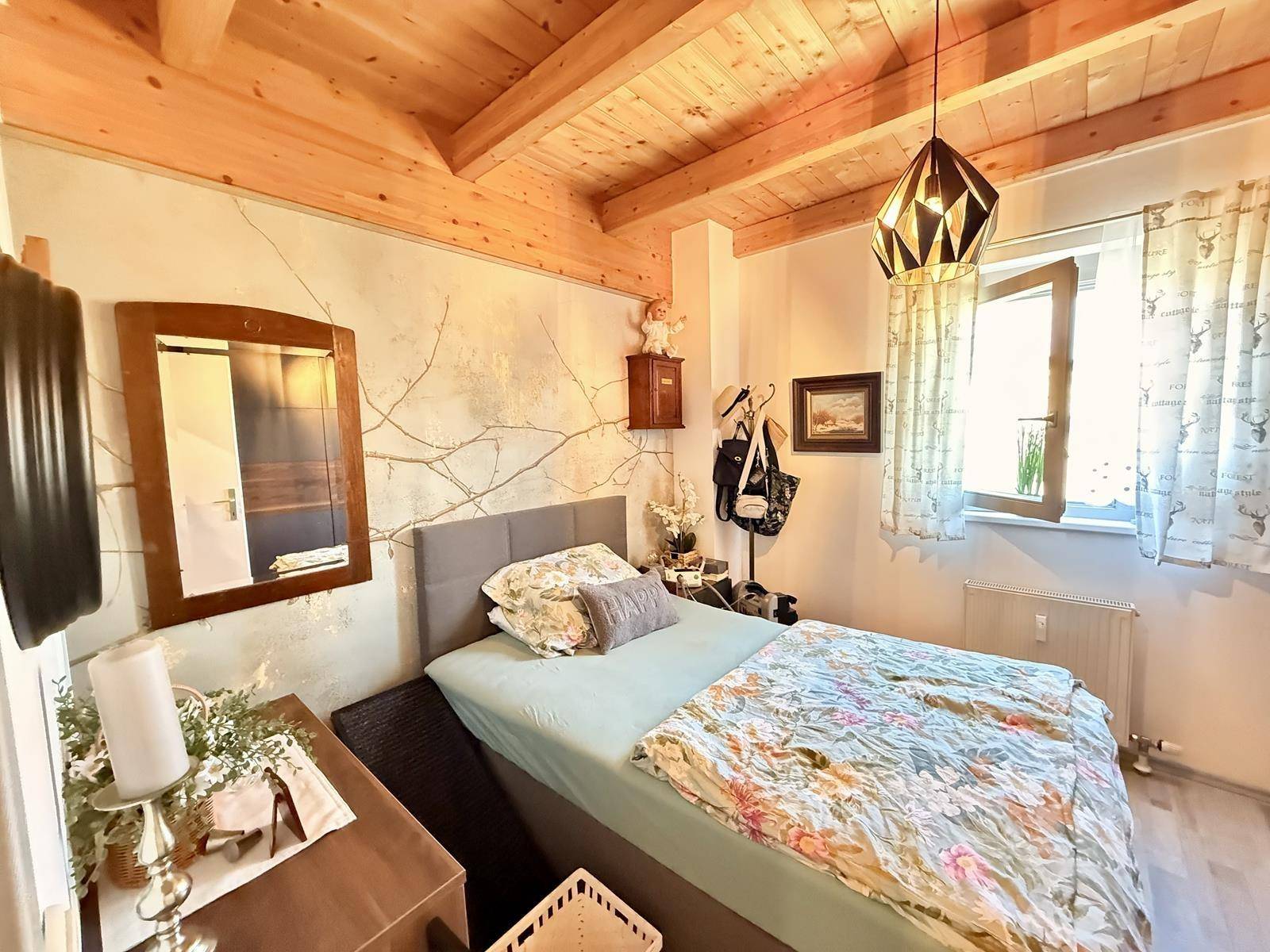 Schlafzimmer mit Holzbalkendecke, gemütlichem Bett und einem Fenster für natürliches Licht.