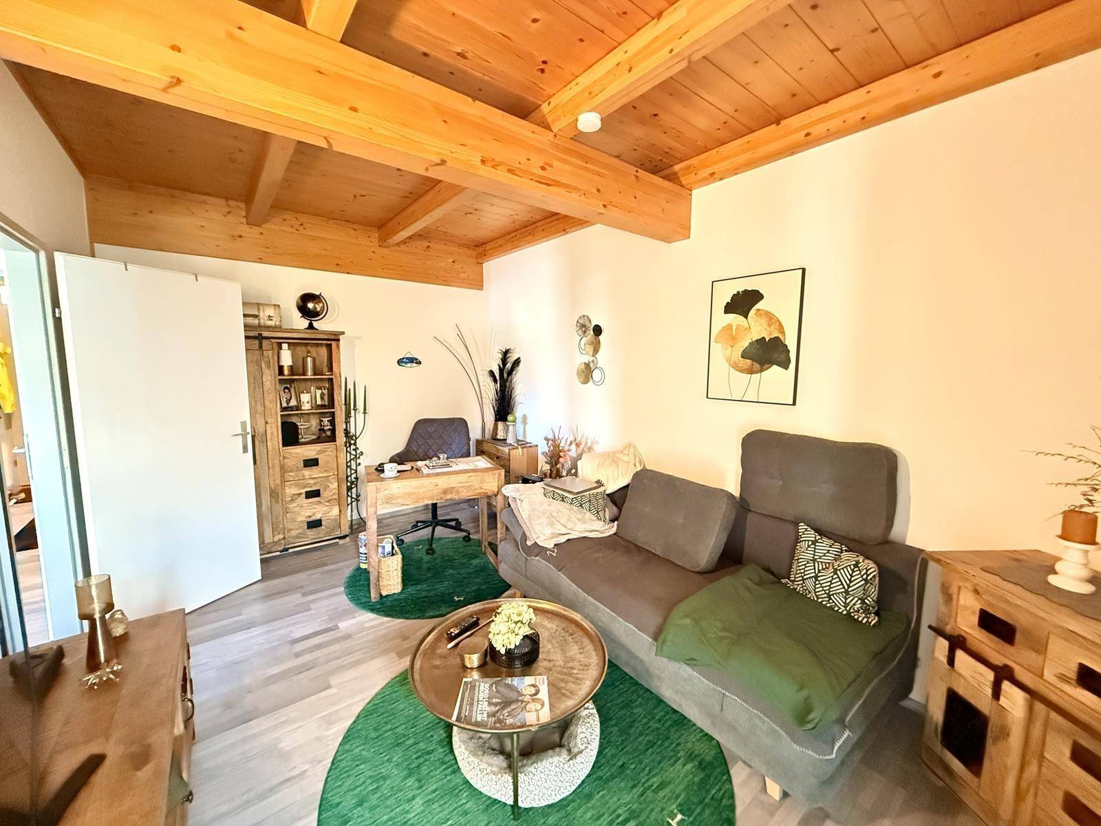 Gemütlicher Wohnbereich mit Sofa und integriertem Arbeitsplatz unter einer Holzbalkendecke.