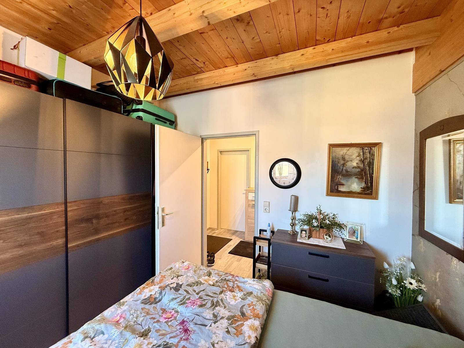 Schlafzimmer mit großem Kleiderschrank, Holzbalkendecke und Zugang zum Flur.