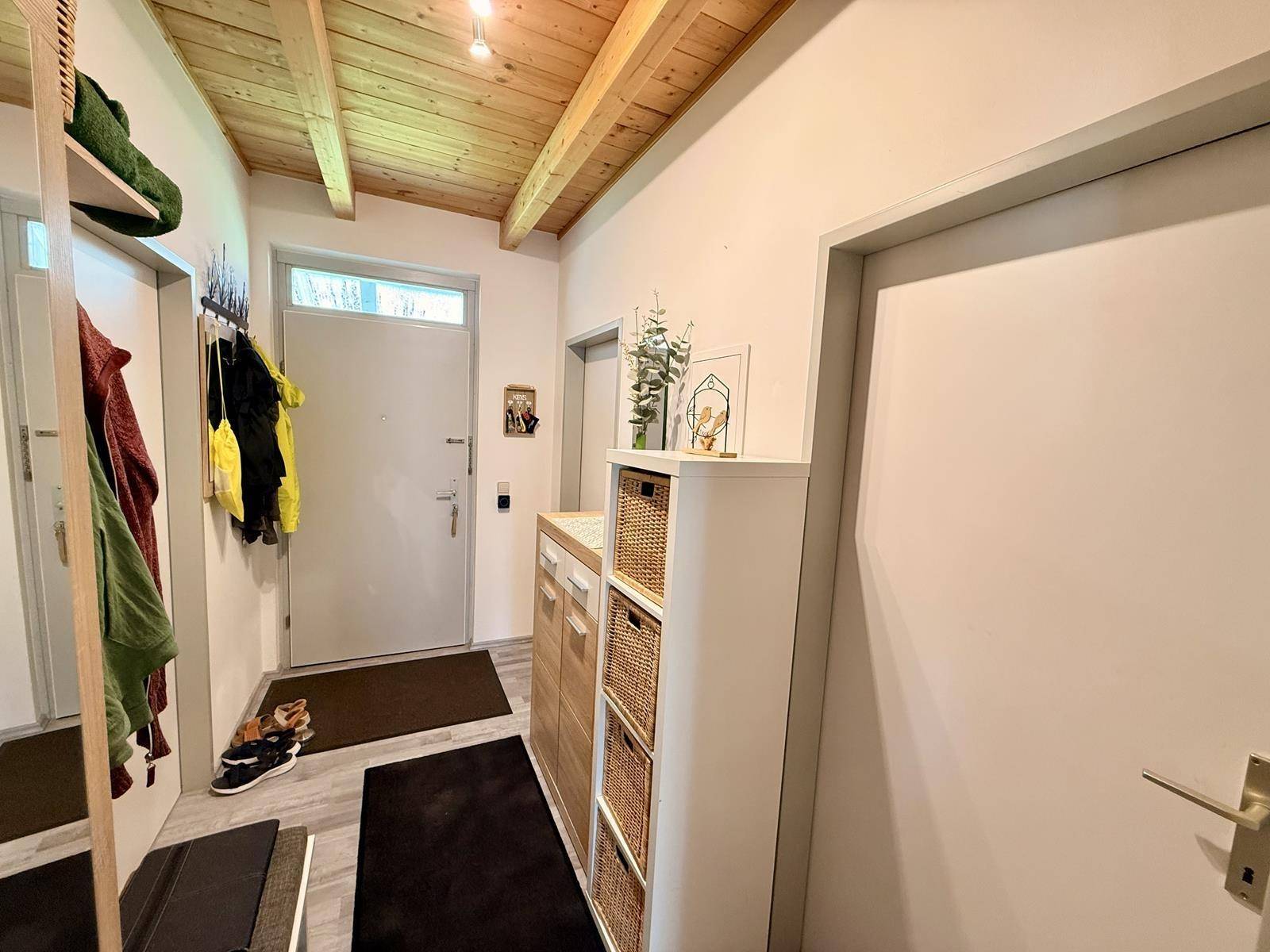 Heller Eingangsbereich mit Garderobe, Schuhschrank und Holzbalkendecke.