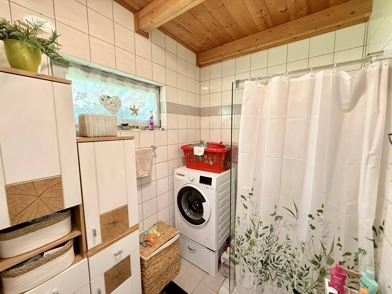 Helles Badezimmer mit Waschmaschine, praktischen Schränken und einem kleinen Fenster.