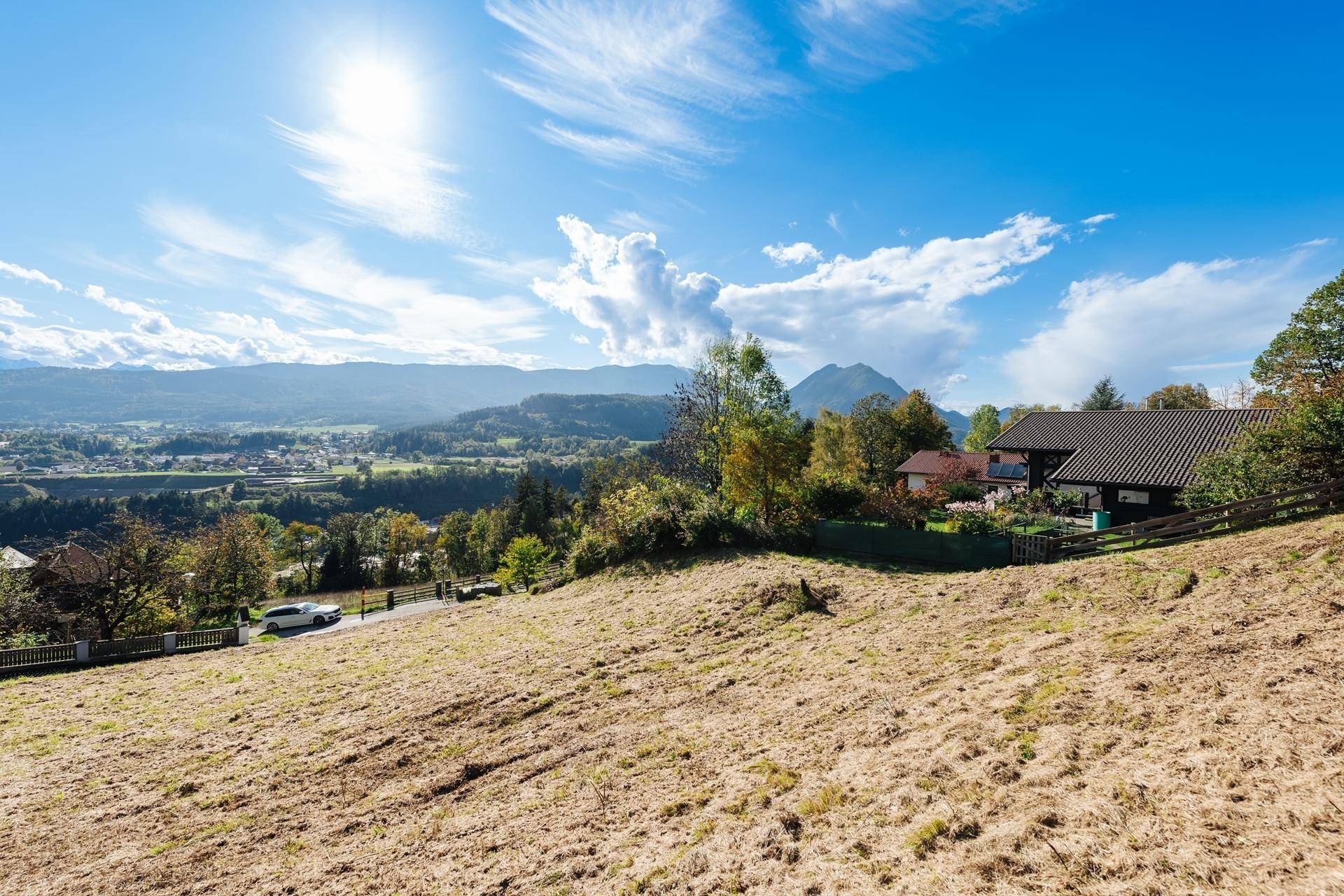 Sonniges Baugrundstück mit Blick auf umliegende Häuser und die beeindruckende Bergkulisse.