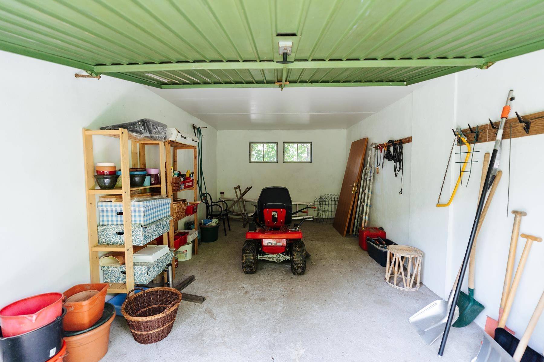 Gut ausgestattete Garage mit Regalen, Werkzeugen und einem Rasenmäher-Traktor.