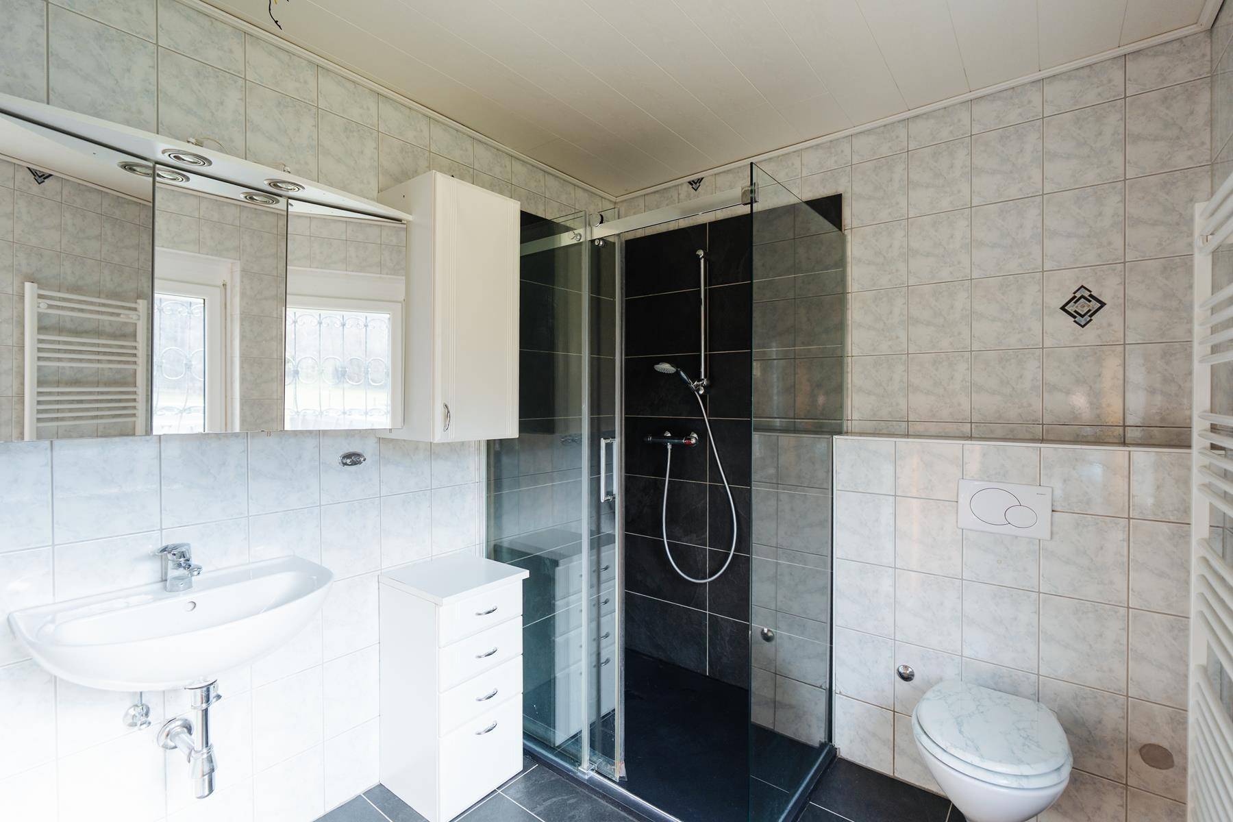 Gefliestes Badezimmer mit Dusche, Waschbecken, Spiegelschrank und beheiztem Handtuchhalter.