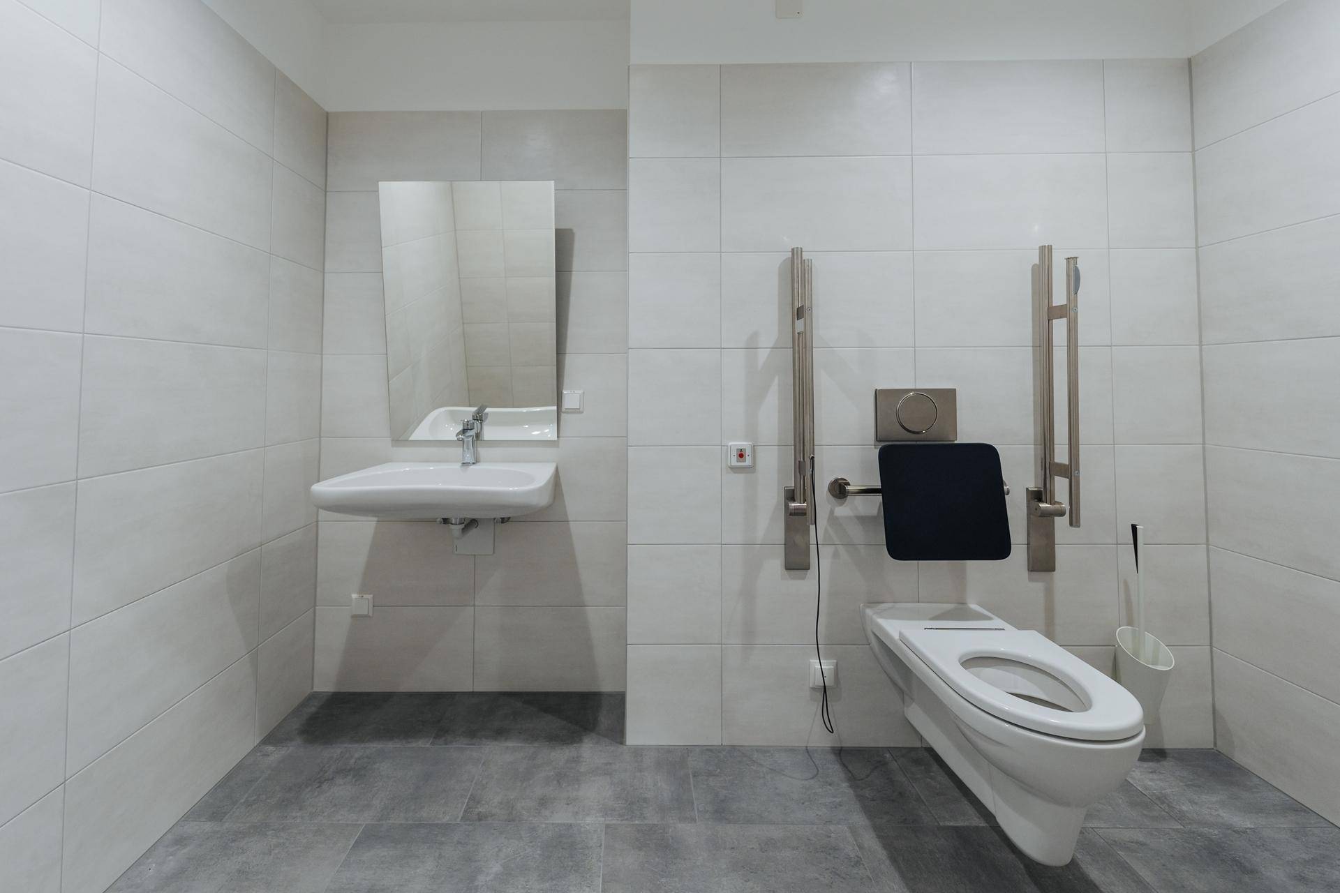 Barrierefreies Badezimmer mit Haltegriffen, wandmontierter Toilette und modernem Waschbecken.