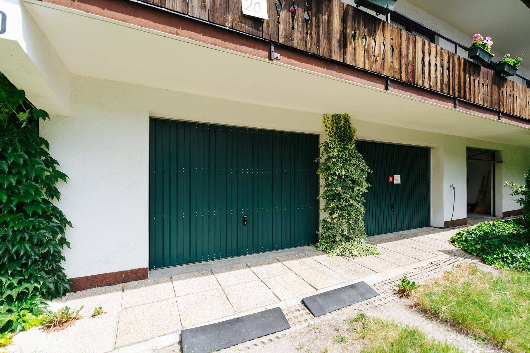 Grüne Garagentore an der Gebäudefassade mit Rankpflanzen und einem darüberliegenden Holzbalkon.