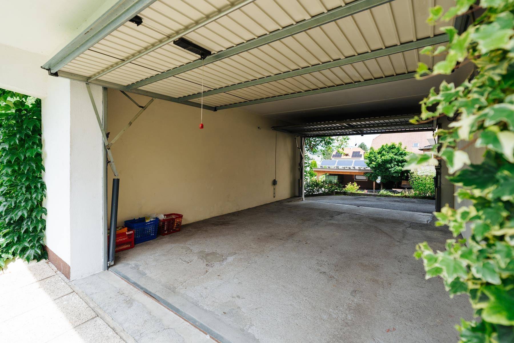 Offene Garage mit Betonboden und Blick ins Grüne, einige Gegenstände sind am Rand abgestellt.