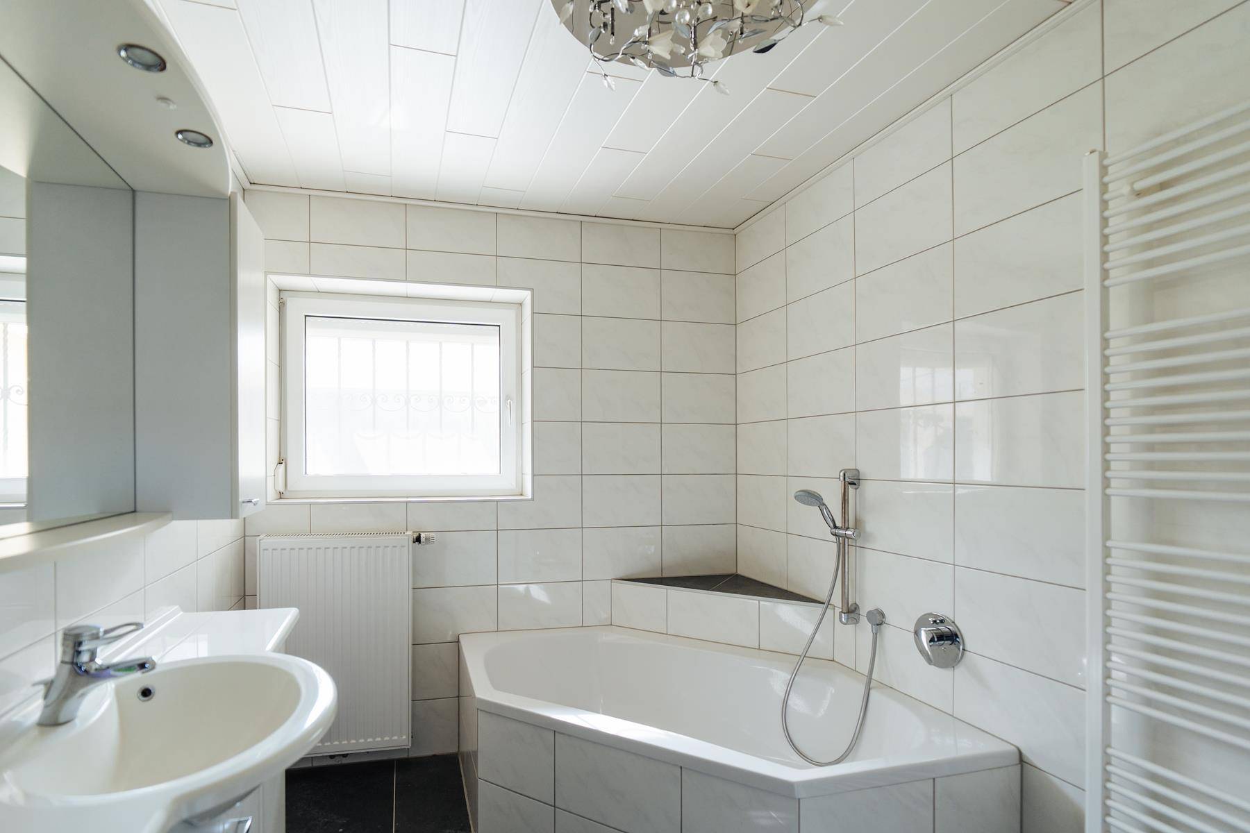Helles Badezimmer mit Eckbadewanne, weißen Fliesen und Fenster.