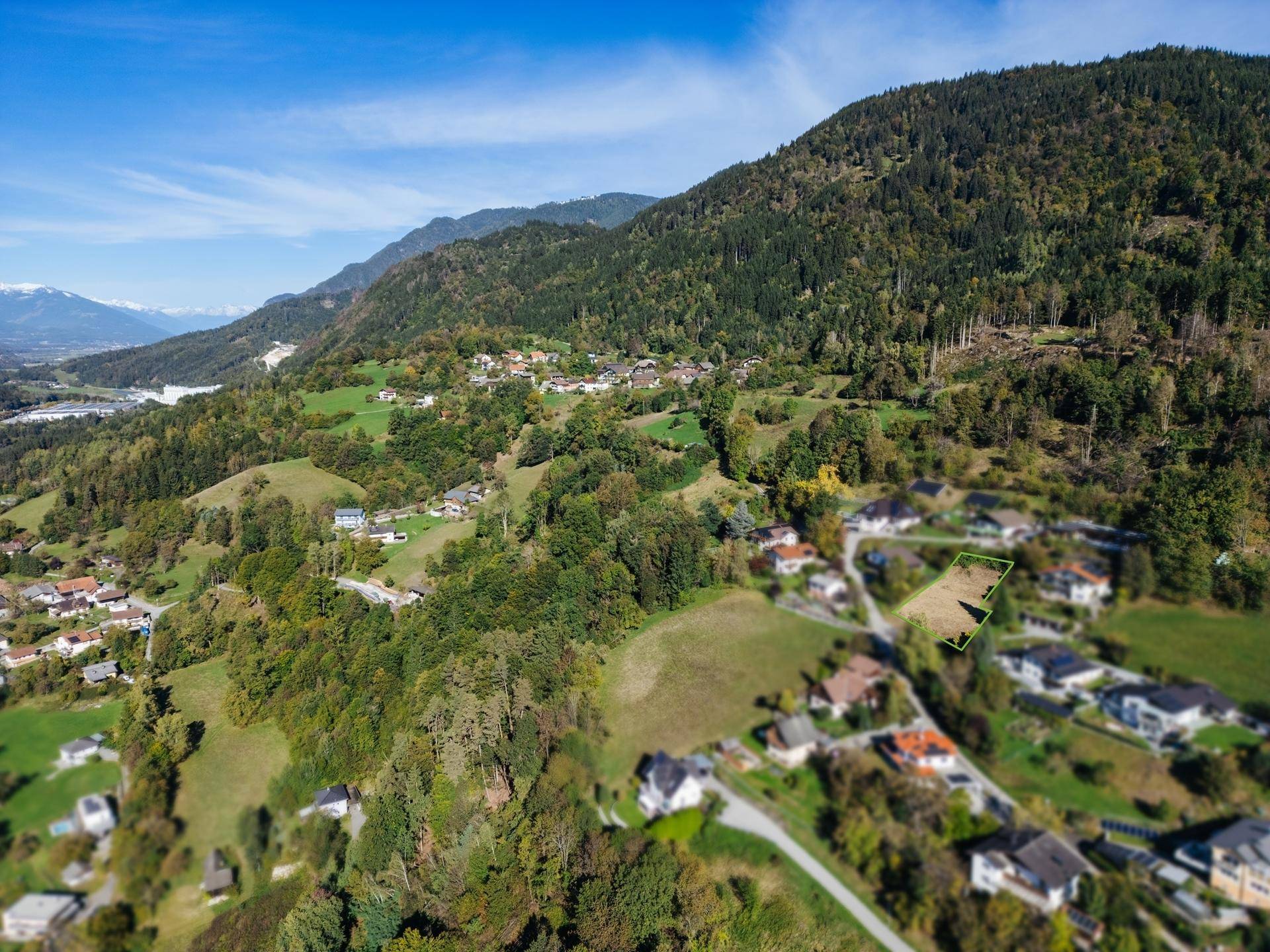 Luftbild des Baugrundstücks mit Blick auf die umliegende Natur und die beeindruckende Bergkette.