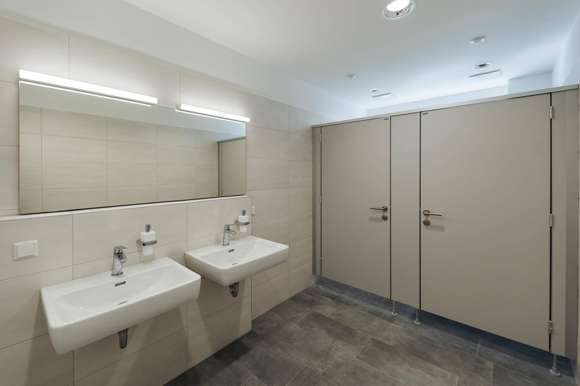 Moderner, sauberer Sanitärbereich mit zwei Waschbecken und mehreren Toilettenkabinen.