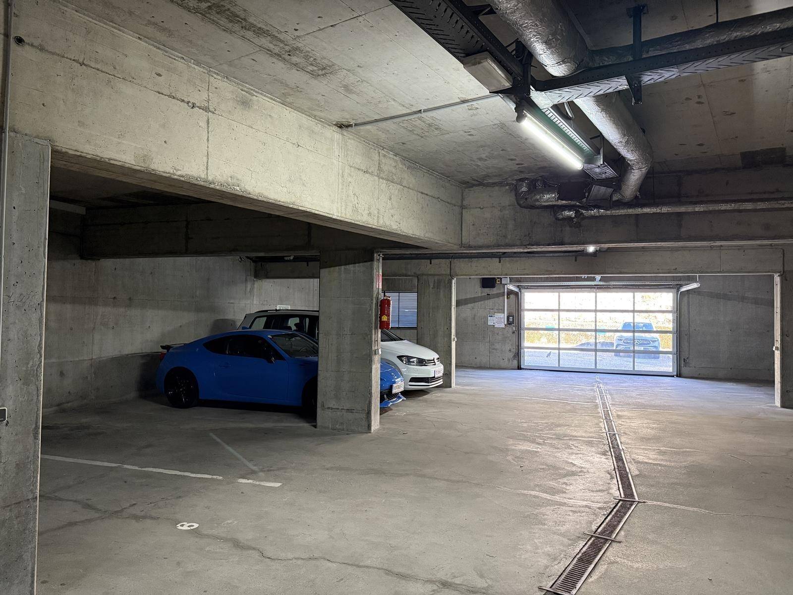 Geräumige Tiefgarage mit Betonwänden und -decken, ausreichend Platz für mehrere Fahrzeuge und gute Beleuchtung.