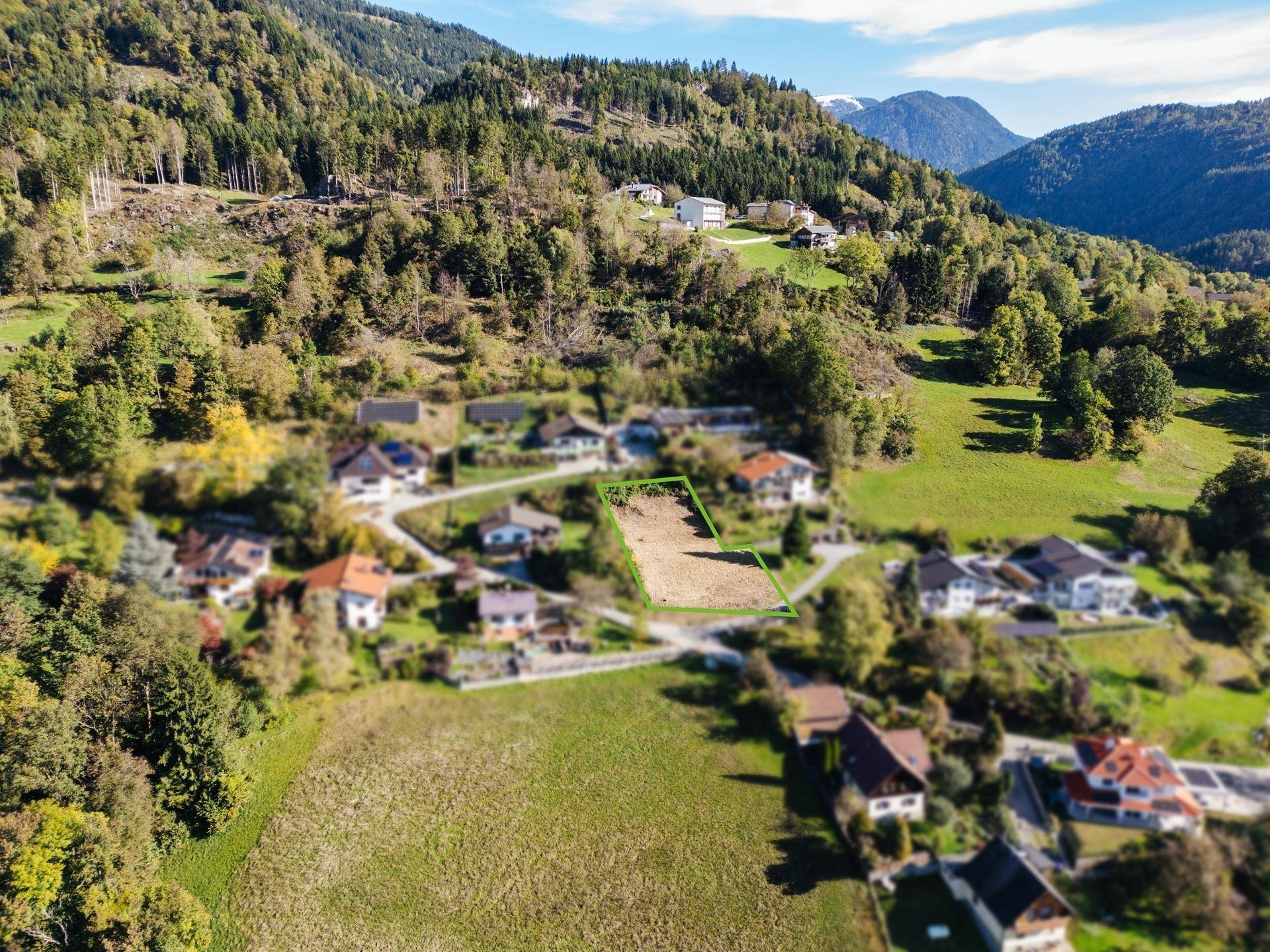 Panoramische Luftaufnahme des Baugrundstücks, eingebettet in eine grüne Hügellandschaft mit Bergen.