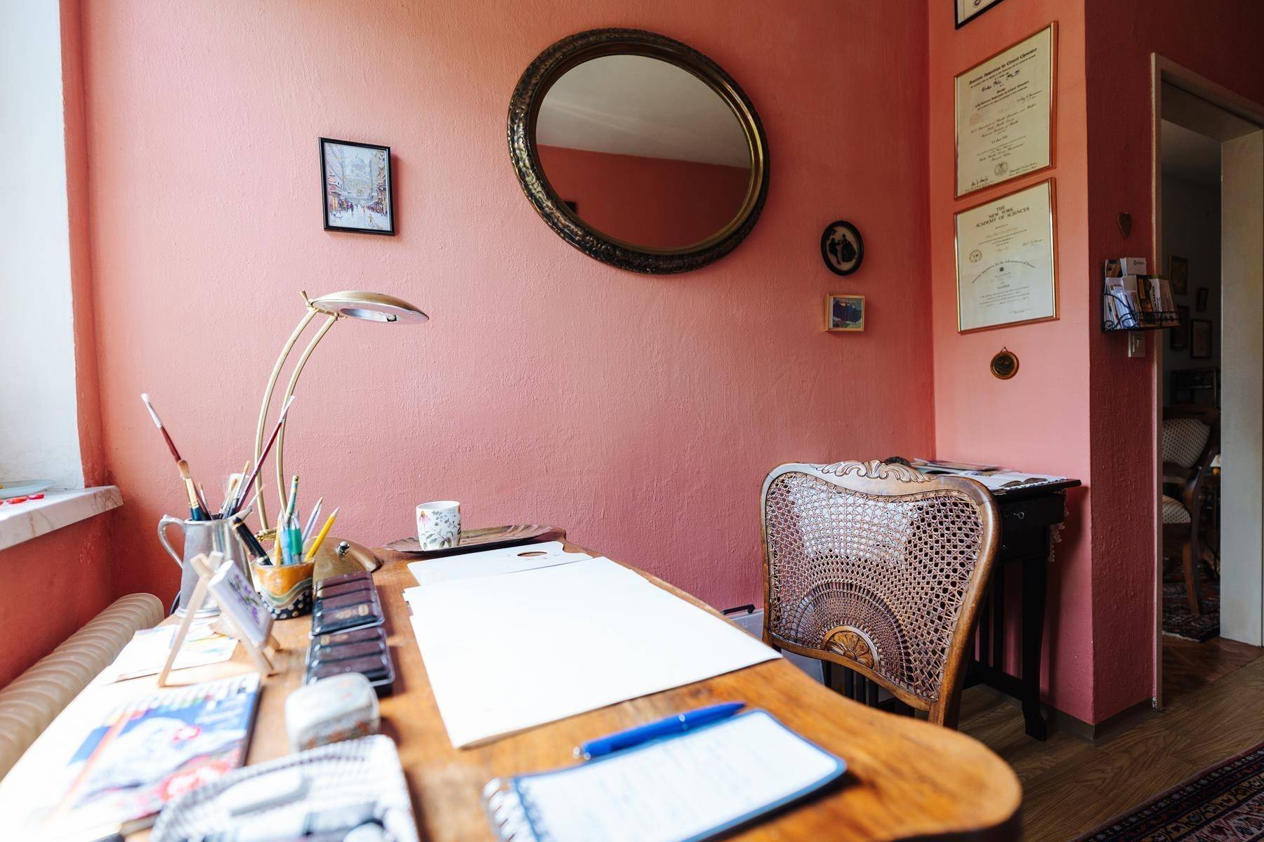 Detailansicht eines Schreibtisches mit Lampe und ovalem Spiegel an der rosa Wand.