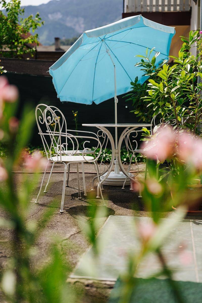 Gemütliche Terrasse mit einem kleinen Tisch, Stühlen und einem blauen Sonnenschirm.