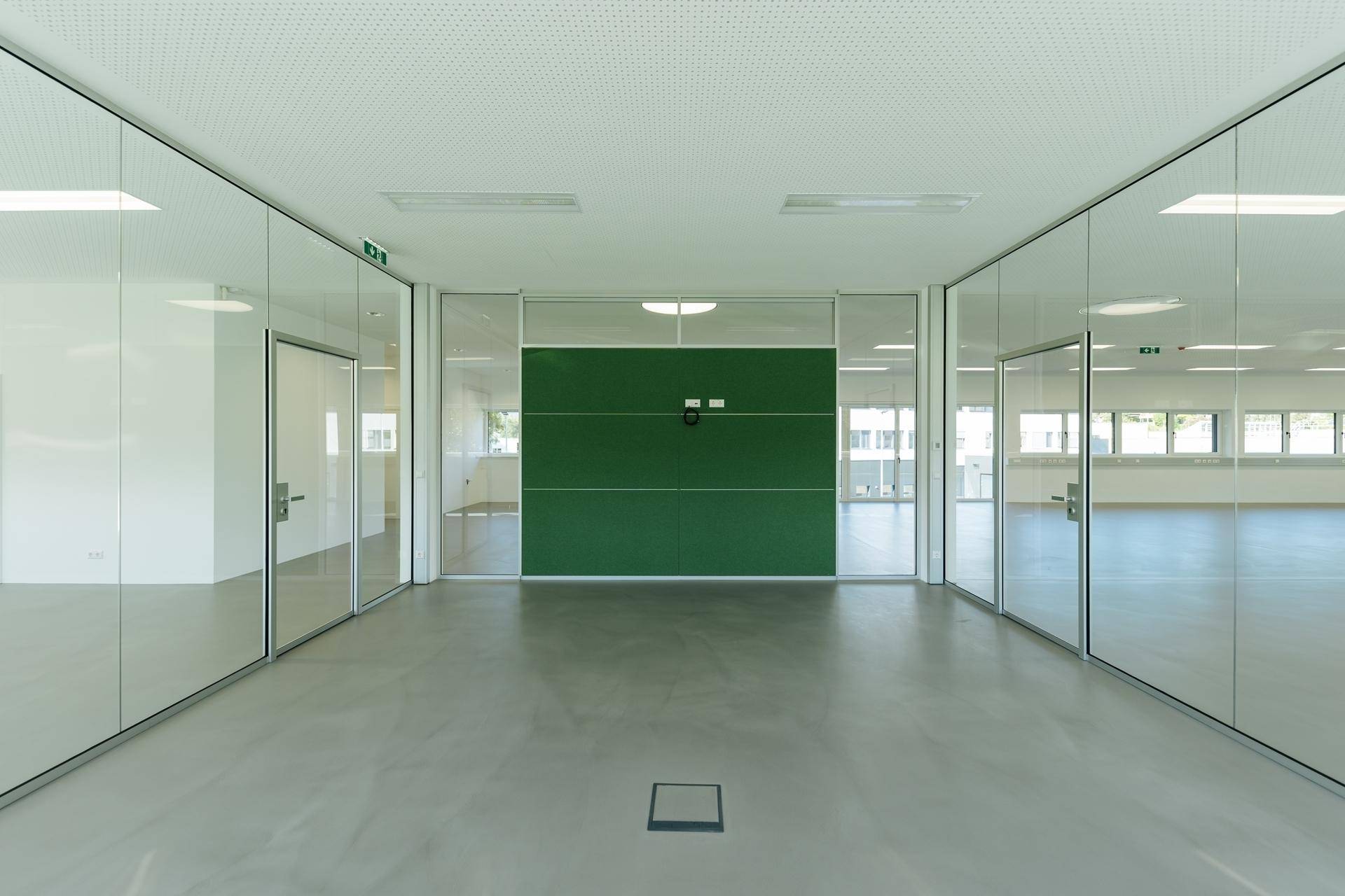 Moderner Bürobereich mit Glaswänden und einer grünen Akzentwand, ideal für Besprechungsräume.