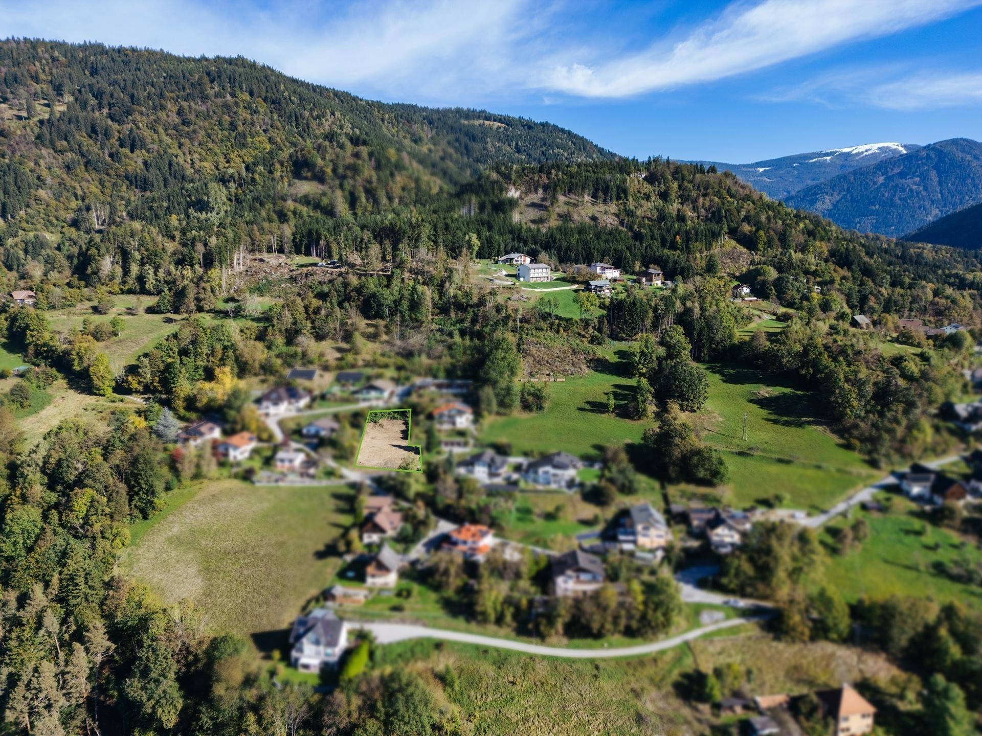 Weitläufige Luftaufnahme des Baugrundstücks in einer Berglandschaft mit umliegenden Häusern.