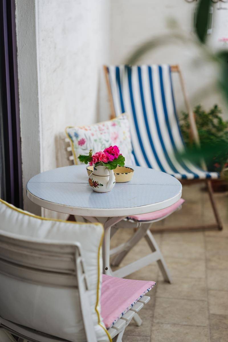 Gemütliche Sitzecke auf dem Balkon mit Blumen und gestreiften Stühlen.