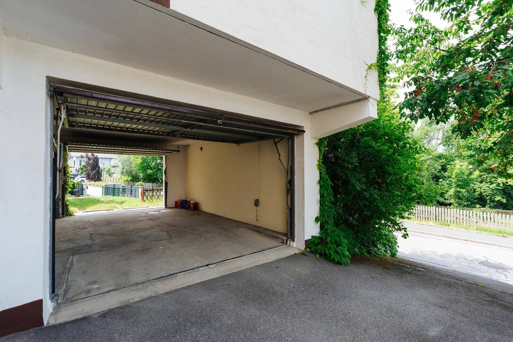 Offene Garage mit Zufahrt und umgebendem Grün, die Einfahrt ist asphaltiert.