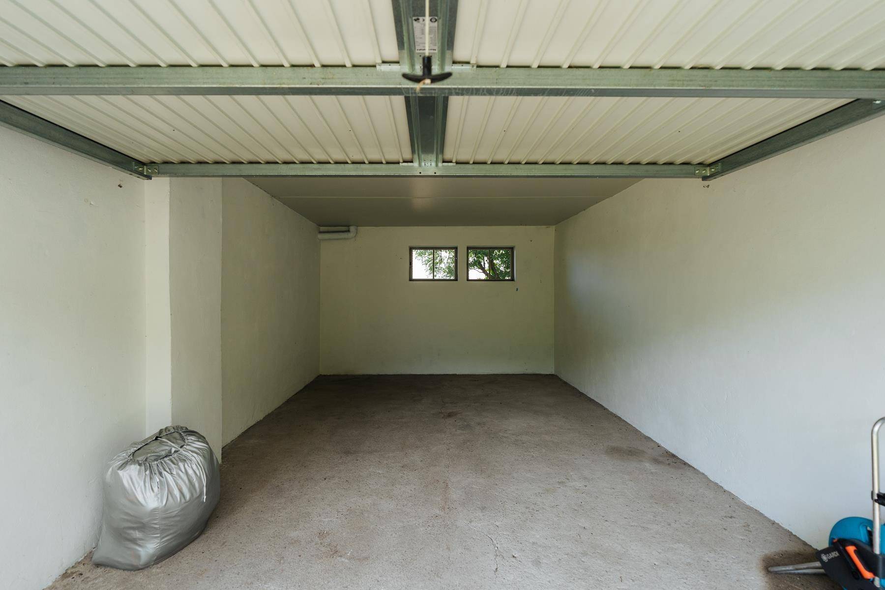 Leere Garage mit Betonboden, weißen Wänden und kleinen Fenstern, bereit zur Nutzung.