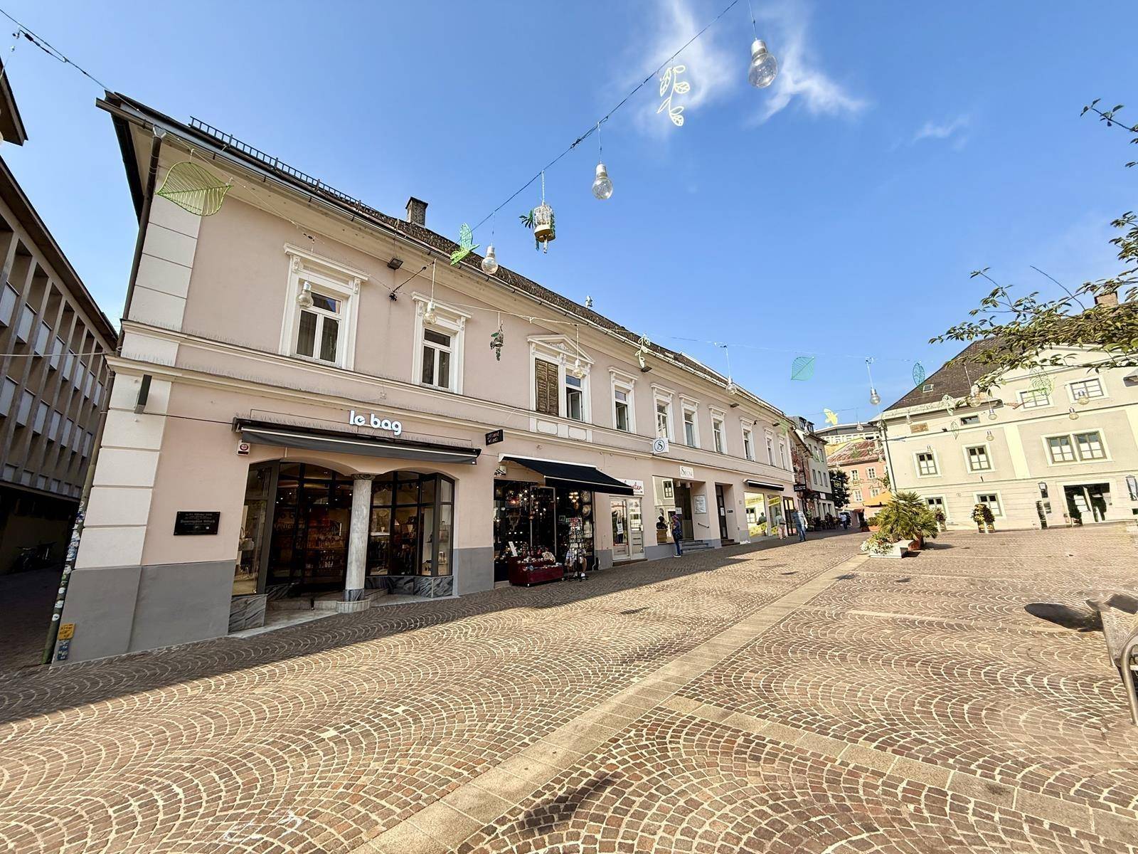 Historische Gebäudezeile mit Geschäften an einem gepflasterten Stadtplatz unter blauem Himmel.