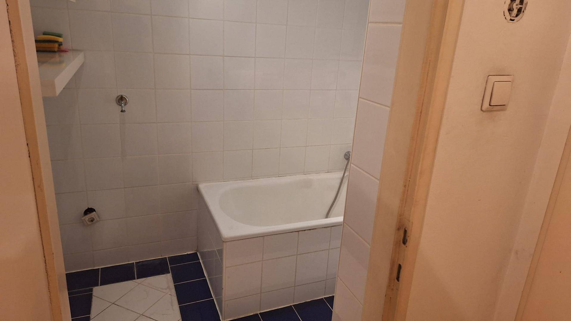 Badezimmer mit Badewanne und weißen Fliesen, bereit für eine Modernisierung.
