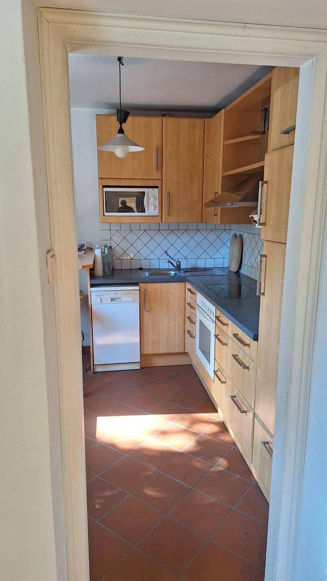 Funktionale Küche mit Holzschränken, Fliesenboden und Einbaugeräten.