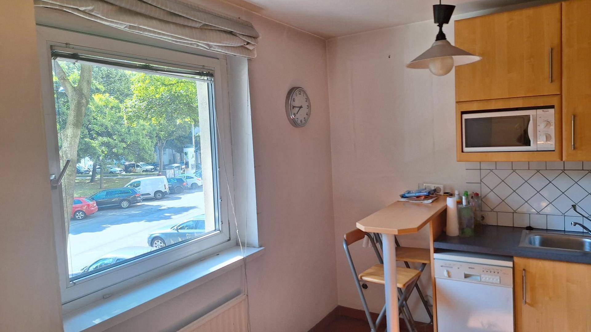 Helle Küche mit Fenster, Holzeinbauten, Frühstücksbar und Blick auf die Straße.