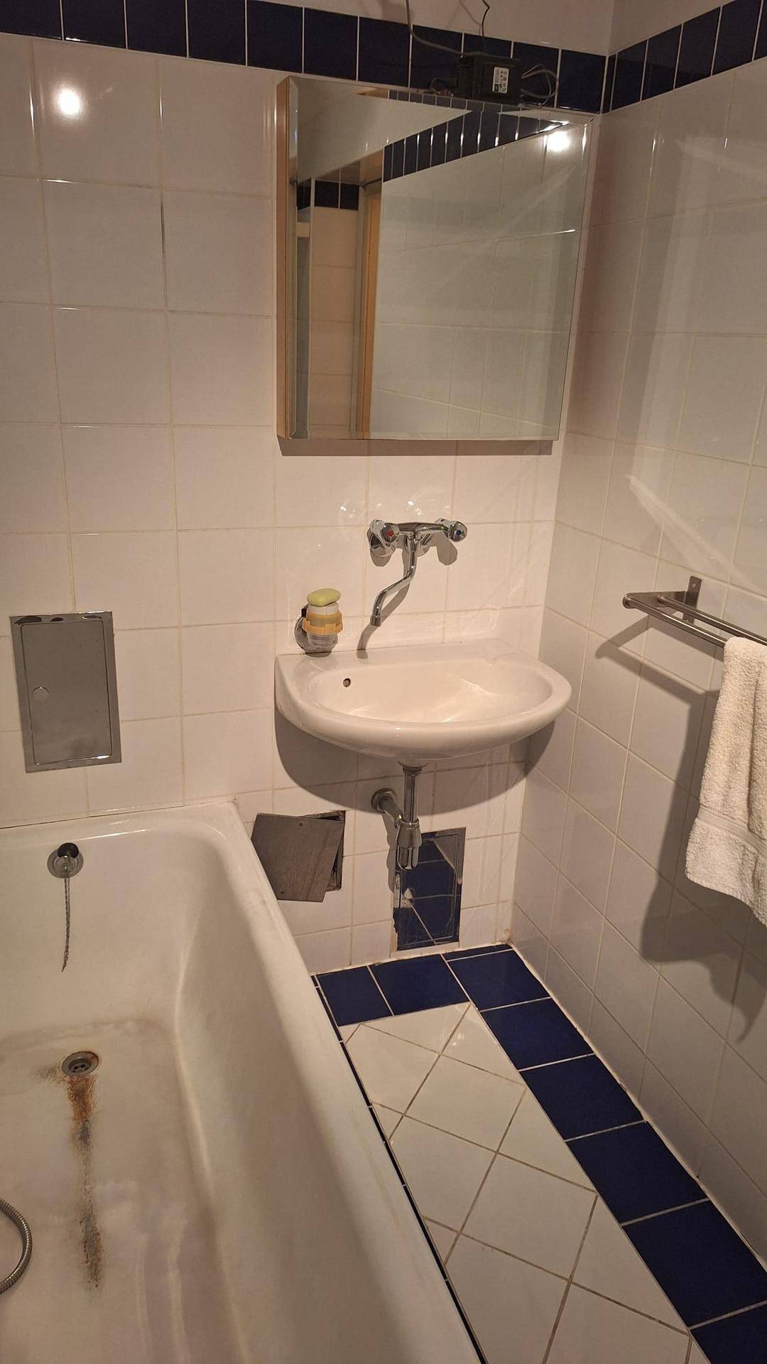 Badezimmer mit Badewanne, Waschbecken und Spiegel, gefliest in Weiß und Blau.